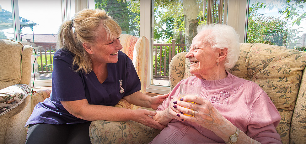 A carer sitting with a resident in the conservatory, holding her hands